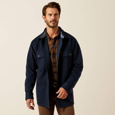 Man wearing a navy blue shacket over a plaid shirt on a beige background